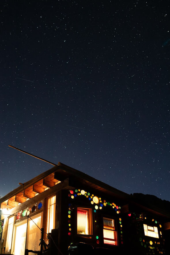 A cozy tiny house adorned with twinkling lights awaits you under a mesmerizing starry sky